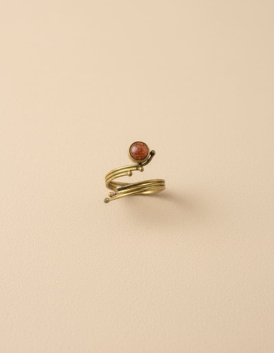 Gold-plated wrap ring with red-orange stone on beige background