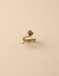 Gold-plated wrap ring with red-orange stone on beige background