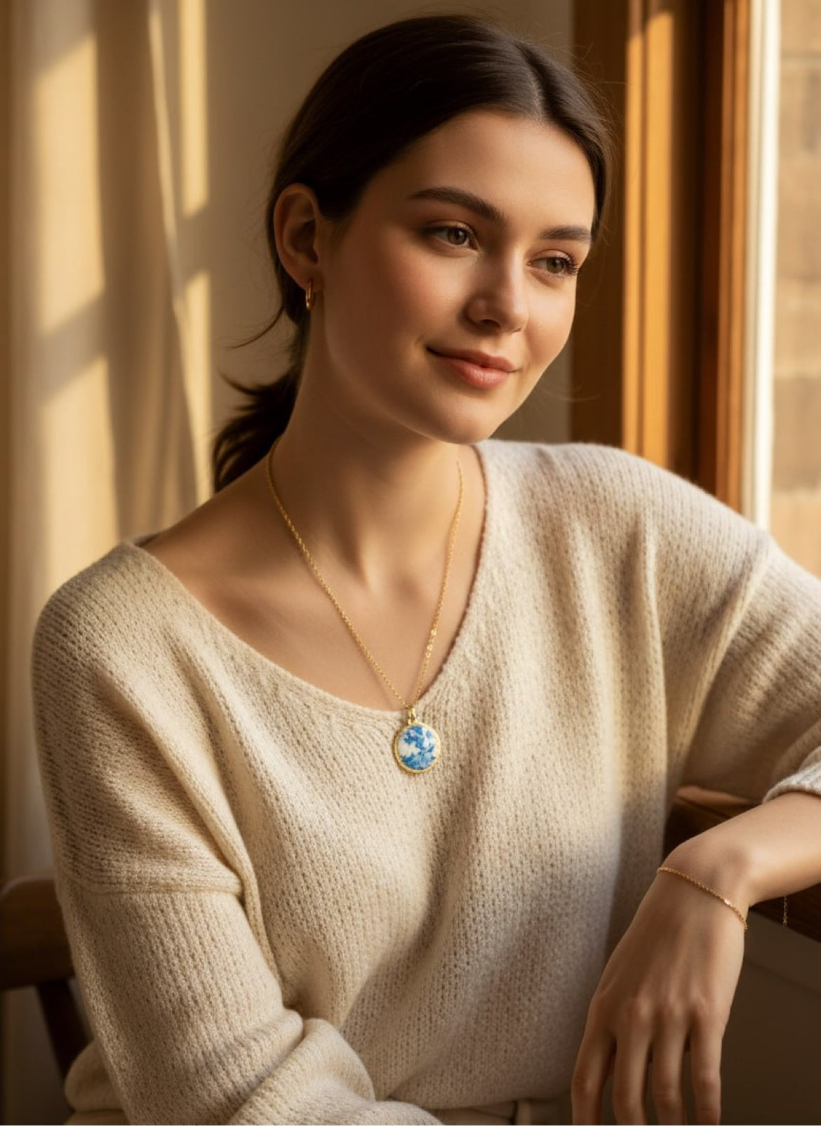 Woman in beige sweater wearing a round blue-and-white enamel pendant necklace