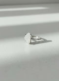 Silver-tone ring with an irregular white stone in a prong setting on a light textured surface.