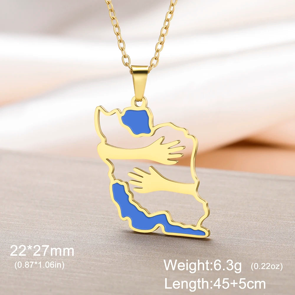Gold pendant necklace featuring a map outline of Iran with two hands hugging, filled with gold, light pink, and blue enamel. The necklace is shown on a gold chain against a soft beige background with text overlays detailing its dimensions and weight.