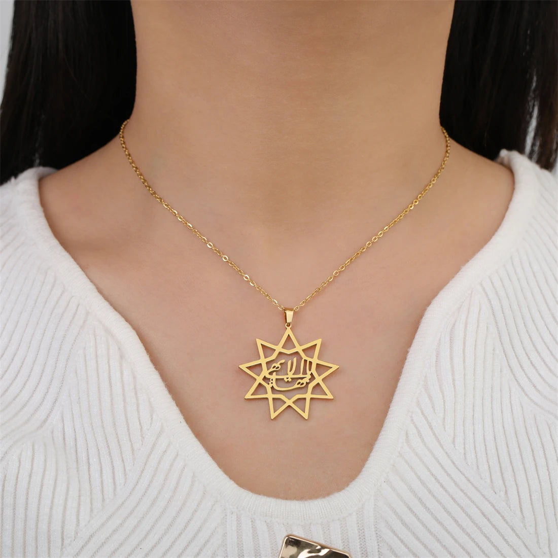 Gold necklace with a star-shaped pendant worn by a person in a white sweater.