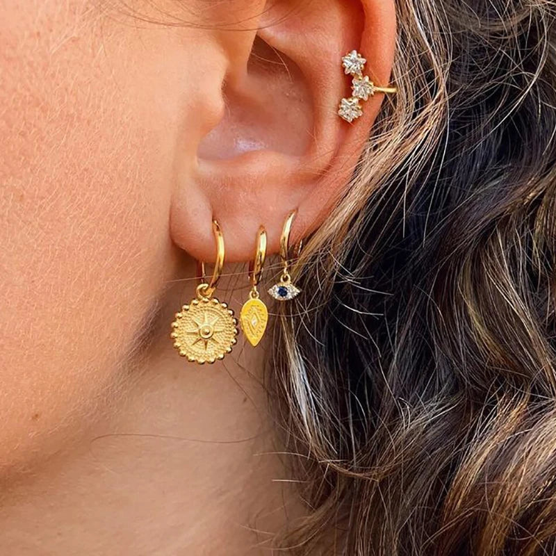 Close-up of an ear wearing gold earrings with various designs.