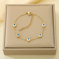 A gold chain bracelet with five evil eye charms, displayed on a beige jewelry box.