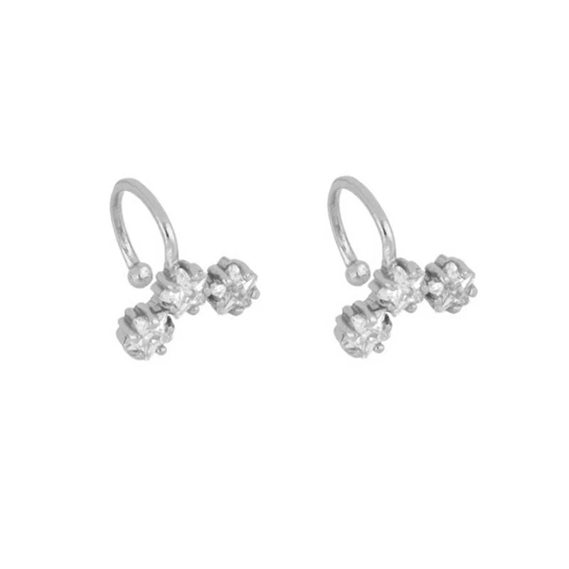 A pair of silver-toned huggie hoop earrings, each adorned with three small clear gemstones clustered at the bottom, shown on a plain white background.