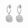 A pair of silver huggie hoop earrings with pavé-set clear stones and a dangling round medallion featuring an engraved lotus flower, shown on a plain white background.