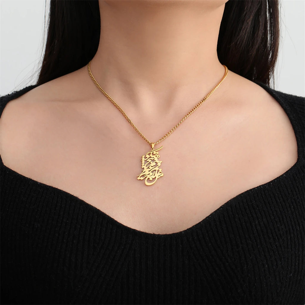 A gold chain necklace with a detailed Arabic calligraphy pendant is shown on a model's neck, wearing a black ribbed top against a light gray background.