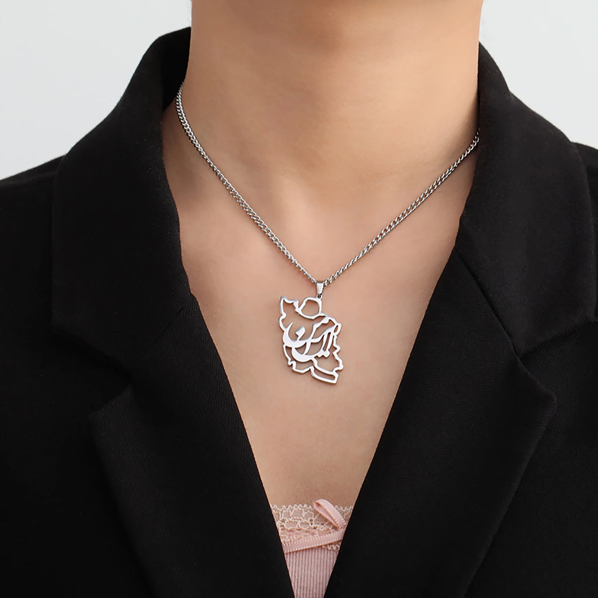 Silver necklace with a leaf-shaped pendant worn by a person in a black blazer.