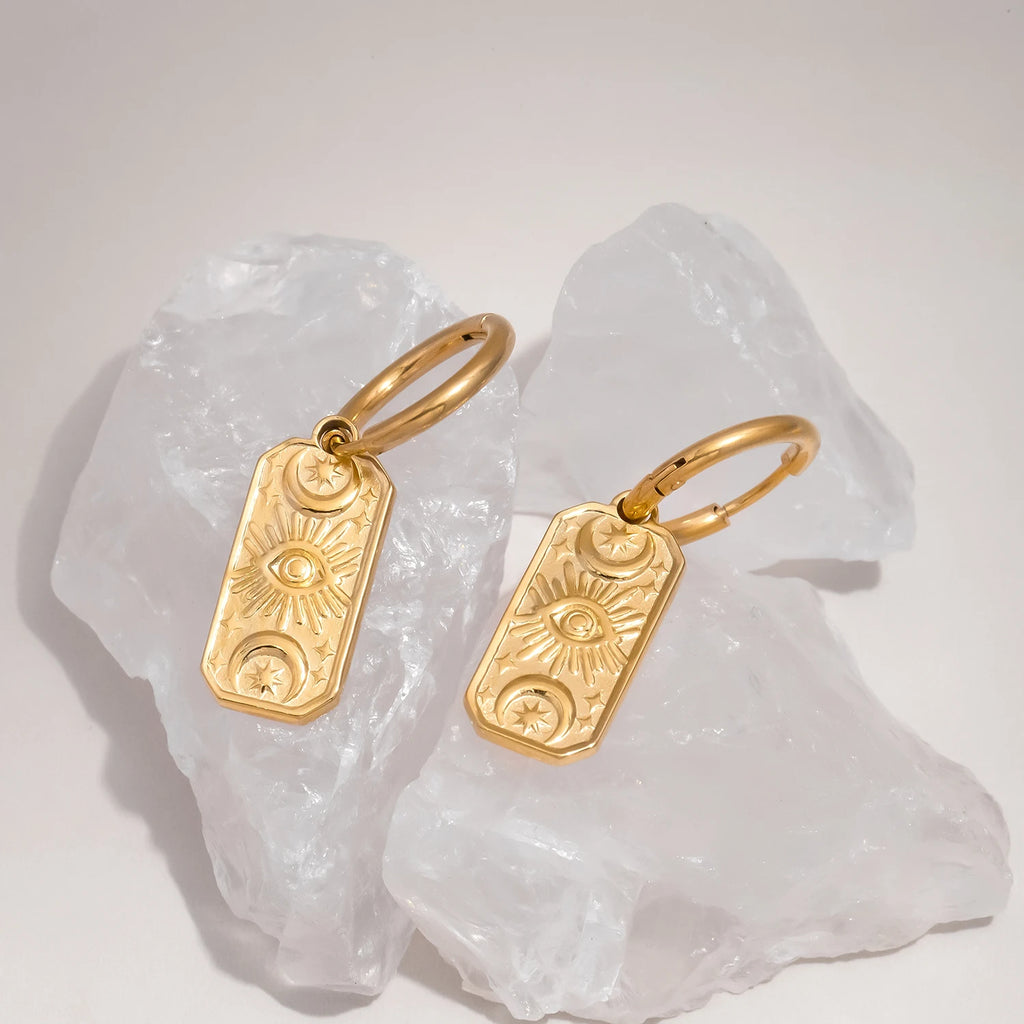 Gold evil eye earrings on white stone background