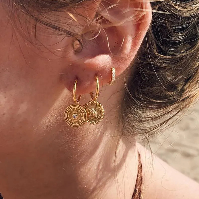 Close-up of a person wearing gold hoop earrings with decorative elements.
