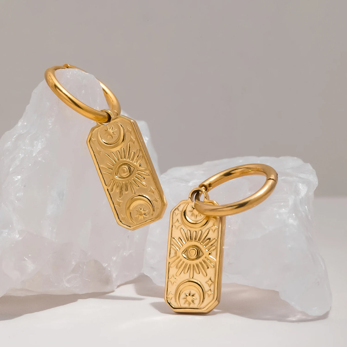 Gold evil eye earrings with sun and moon designs on textured white surface