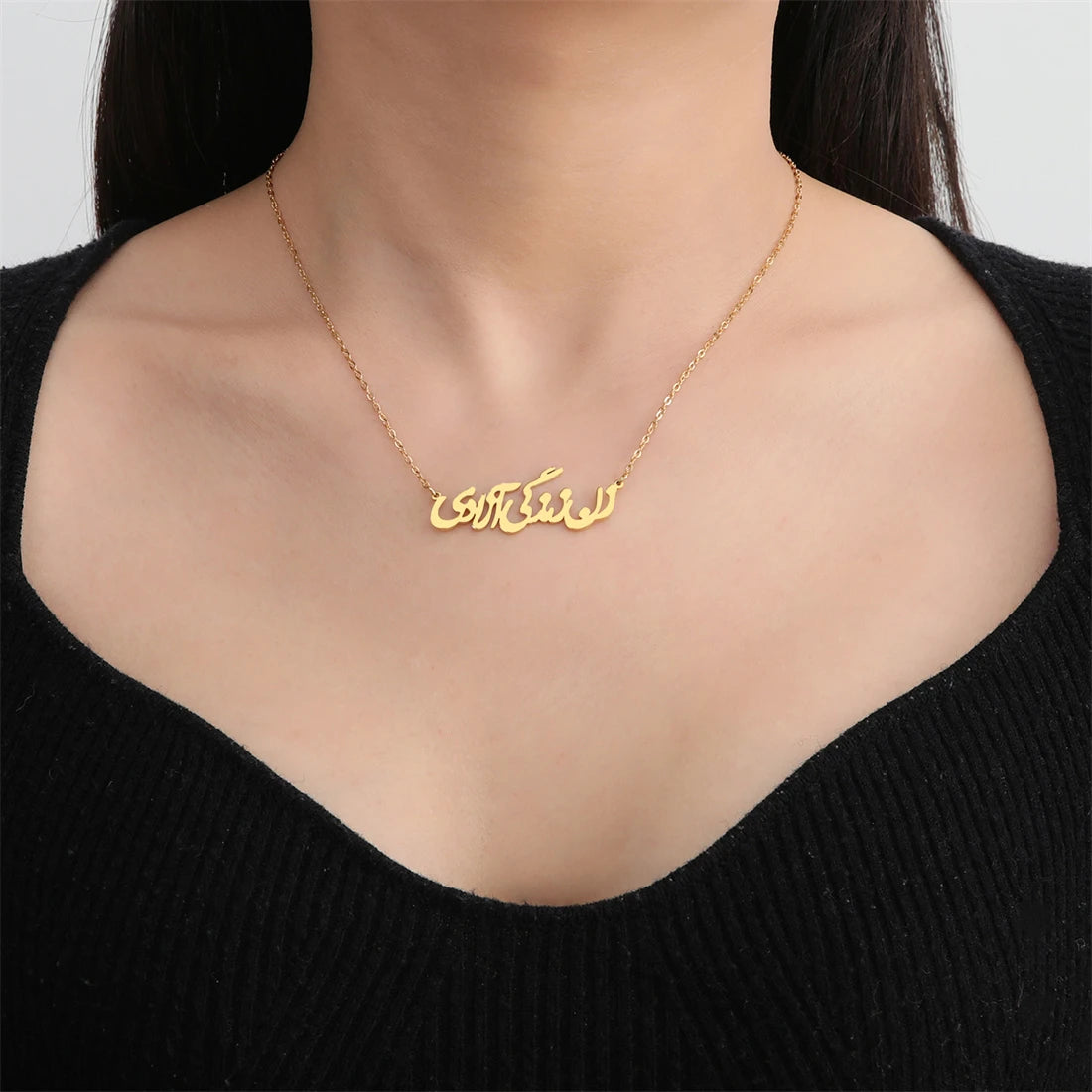 A close-up of a model wearing a delicate gold chain necklace with a custom Arabic nameplate pendant, styled with a black ribbed top.