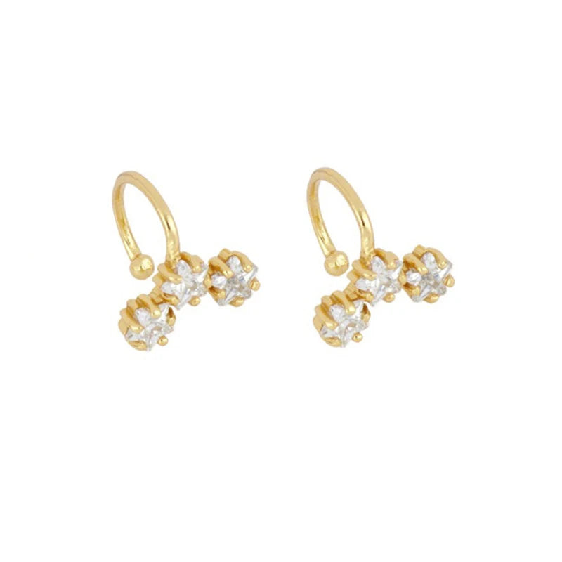 A pair of gold huggie hoop earrings with three clear round-cut gemstones clustered at the bottom of each hoop, shown on a plain white background.