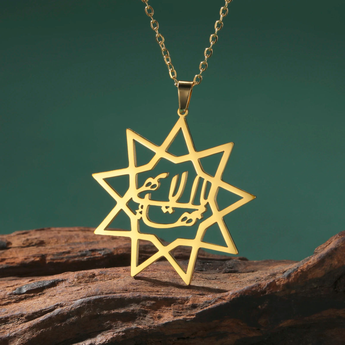 Gold star-shaped pendant with Arabic text on a chain, placed on a rock with a green background