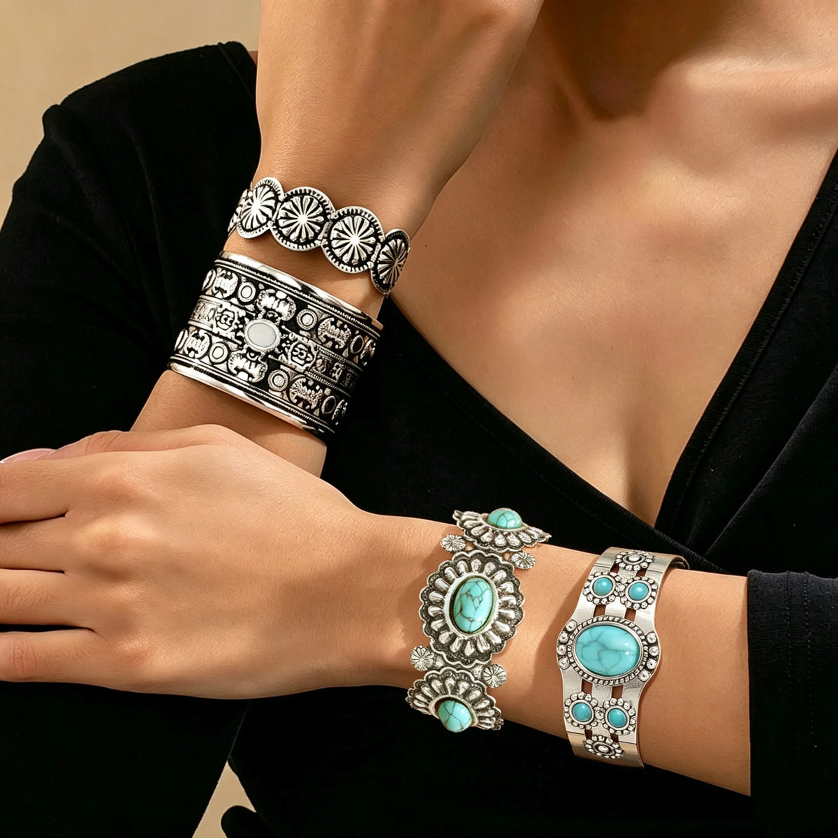 A close-up of a person wearing multiple silver-toned cuff bracelets with turquoise stones and engraved patterns, paired with a black top.