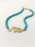 Turquoise beaded necklace with gold-plated calligraphy centerpiece on white