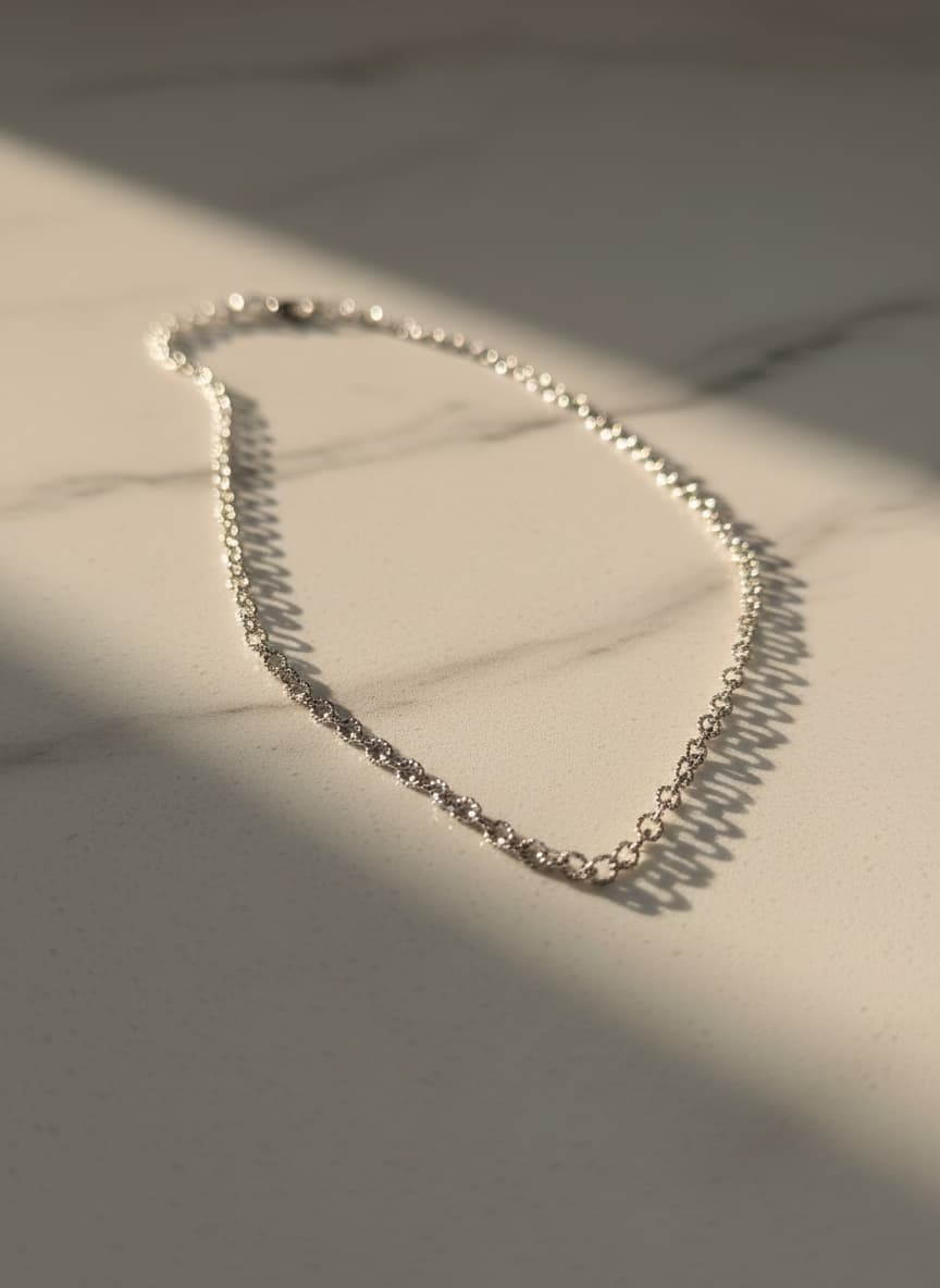 Silver-tone textured link chain necklace on marble in sunlight